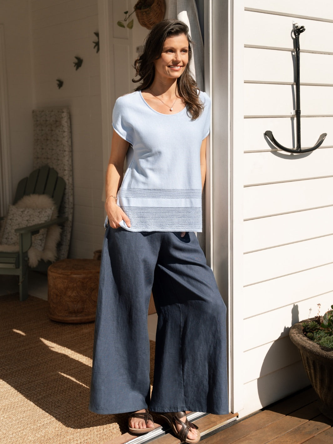 Woman standing on a porch wearing a light blue top and dark blue pants.