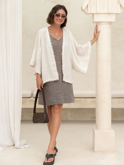 Woman in a gray dress with a white cardigan standing in a bright, minimalistic room.