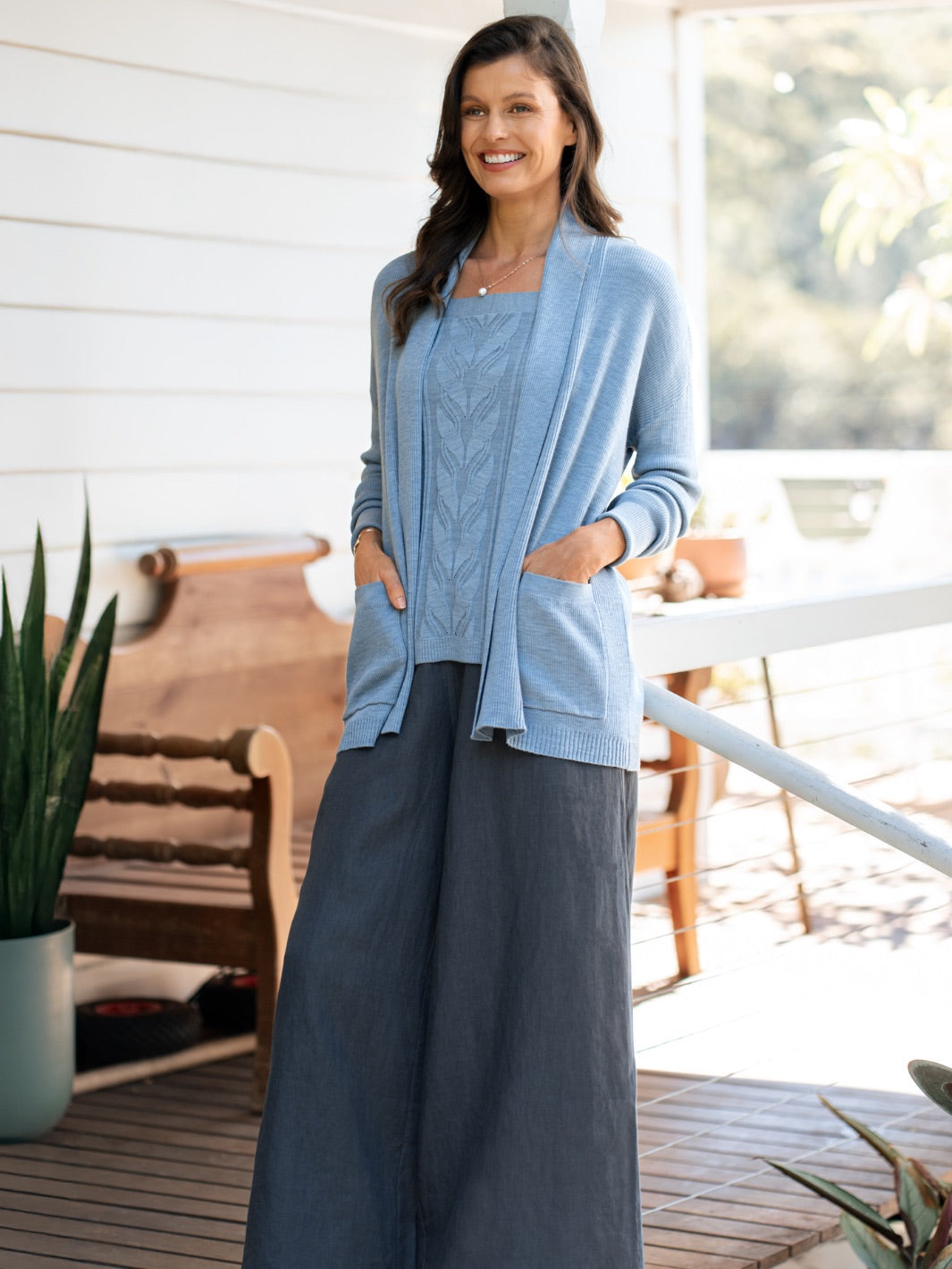 Woman wearing a light blue cardigan over dark pants on a wooden deck.
