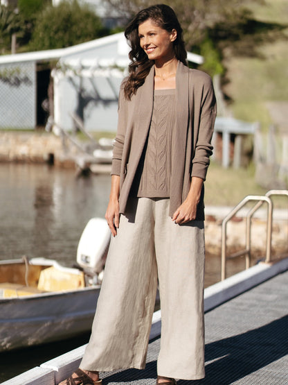 Woman in a brown cardigan and beige pants standing by a waterfront.