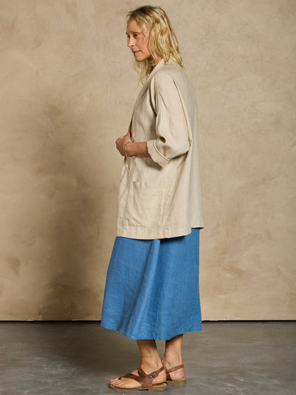Woman in a blue linen dress and beige linen jacket.