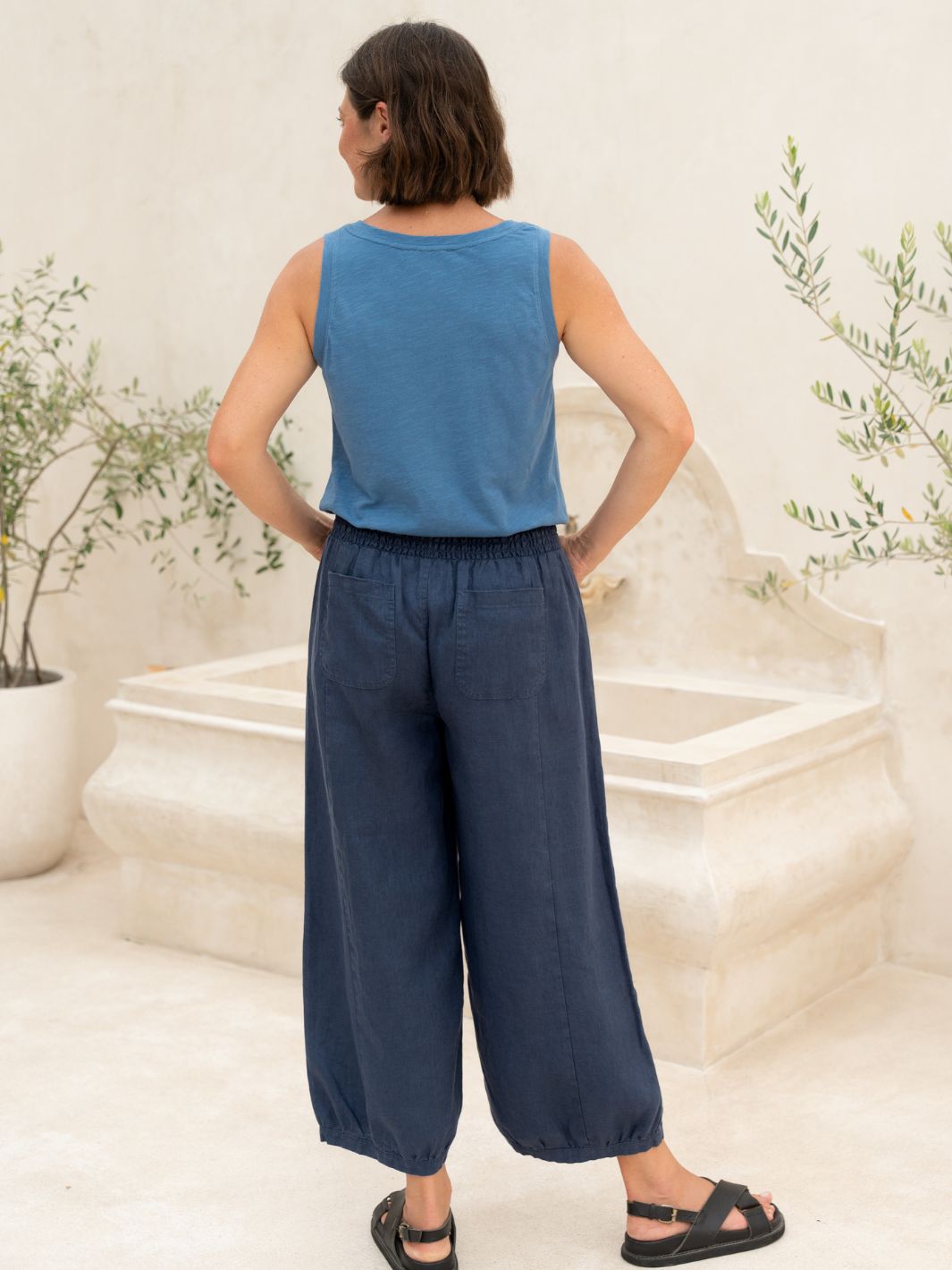 Woman wearing a blue sleeveless top and navy wide-leg pants standing in a decorative indoor setting.