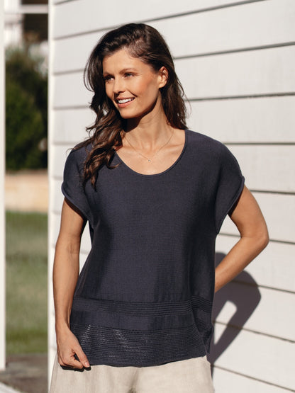 Woman wearing a black top standing outdoors against a white wall.