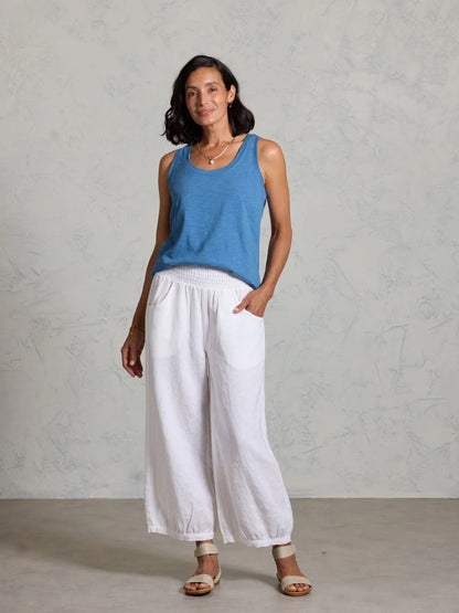 Woman wearing a blue sleeveless top and white pants against a gray background