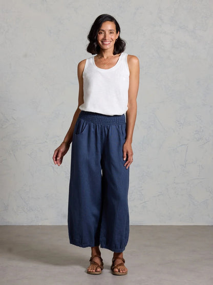 Woman wearing a white sleeveless top and navy wide-leg pants against a gray background