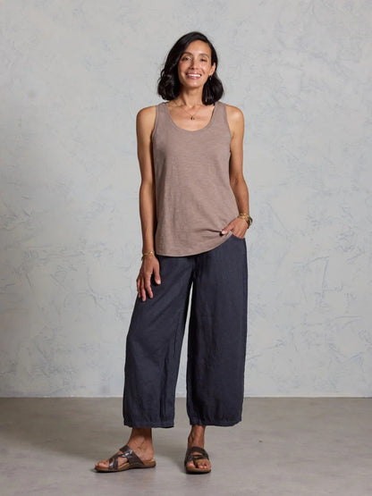 Woman wearing a brown tank top and dark pants against a gray background