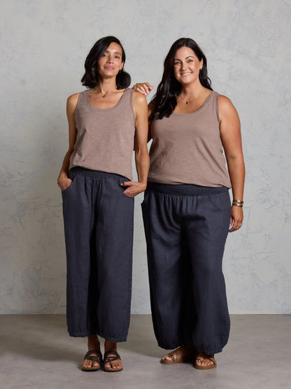 Two women wearing matching brown tank tops and black pants standing against a plain background.